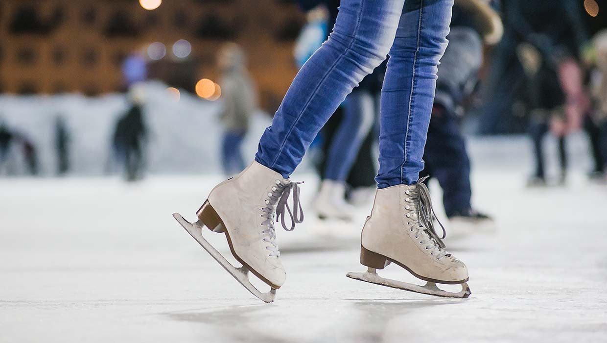 Nahaufnahme von Schlittschuhen auf der Eisbahn mit Besuchern im Hintergrund.